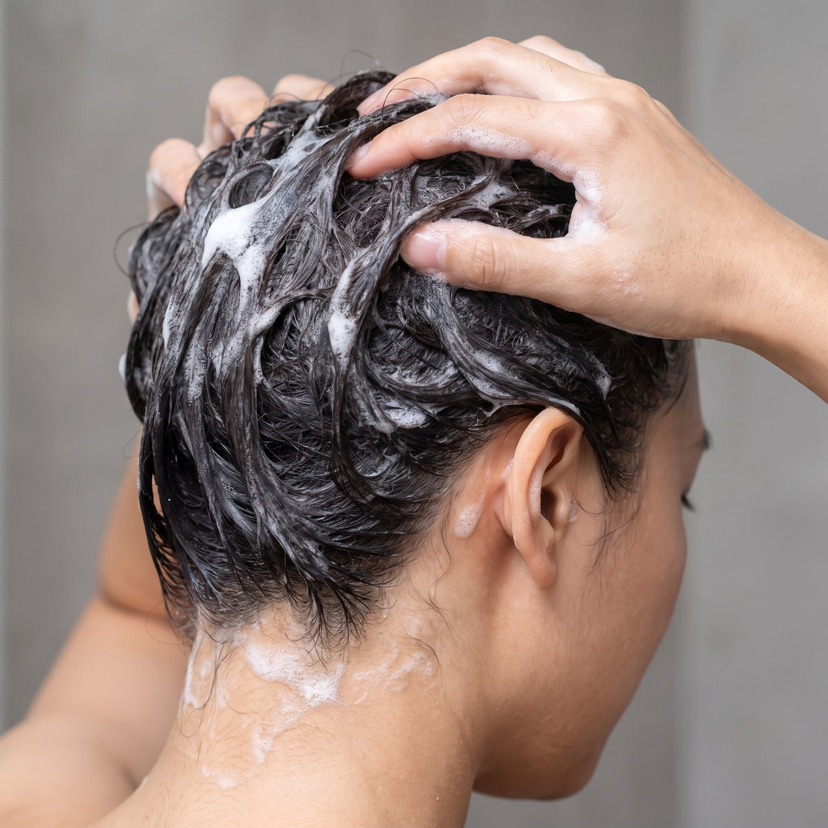 Hands massaging AROMATICA Tea Tree Purifying Shampoo lather into wet dark hair and scalp