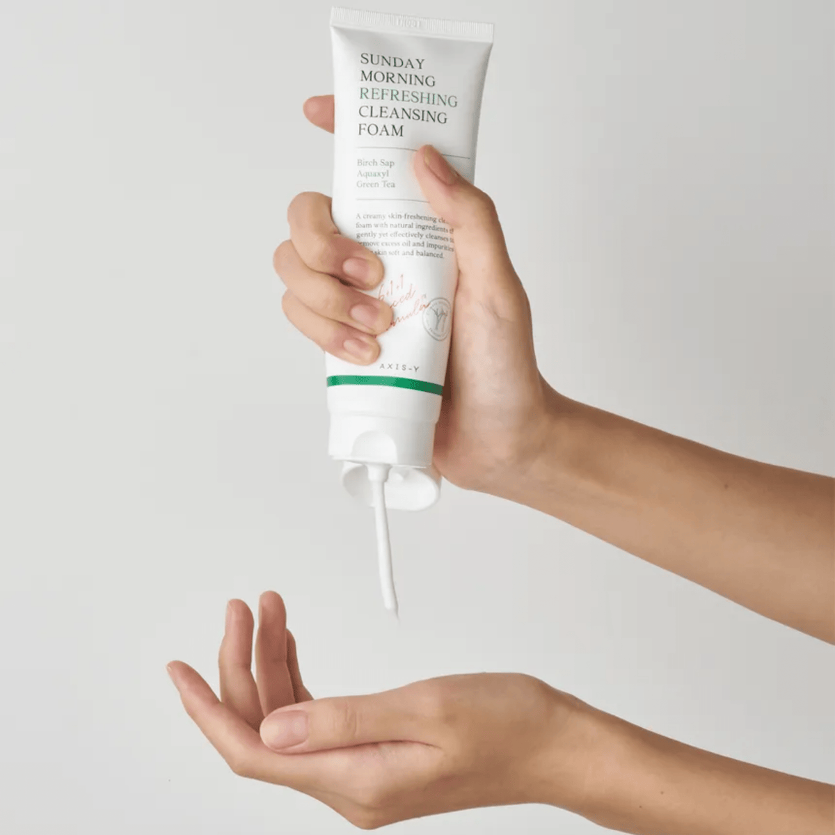 Hands squeezing AXIS-Y Sunday Morning Refreshing Cleansing Foam from the tube onto an open palm