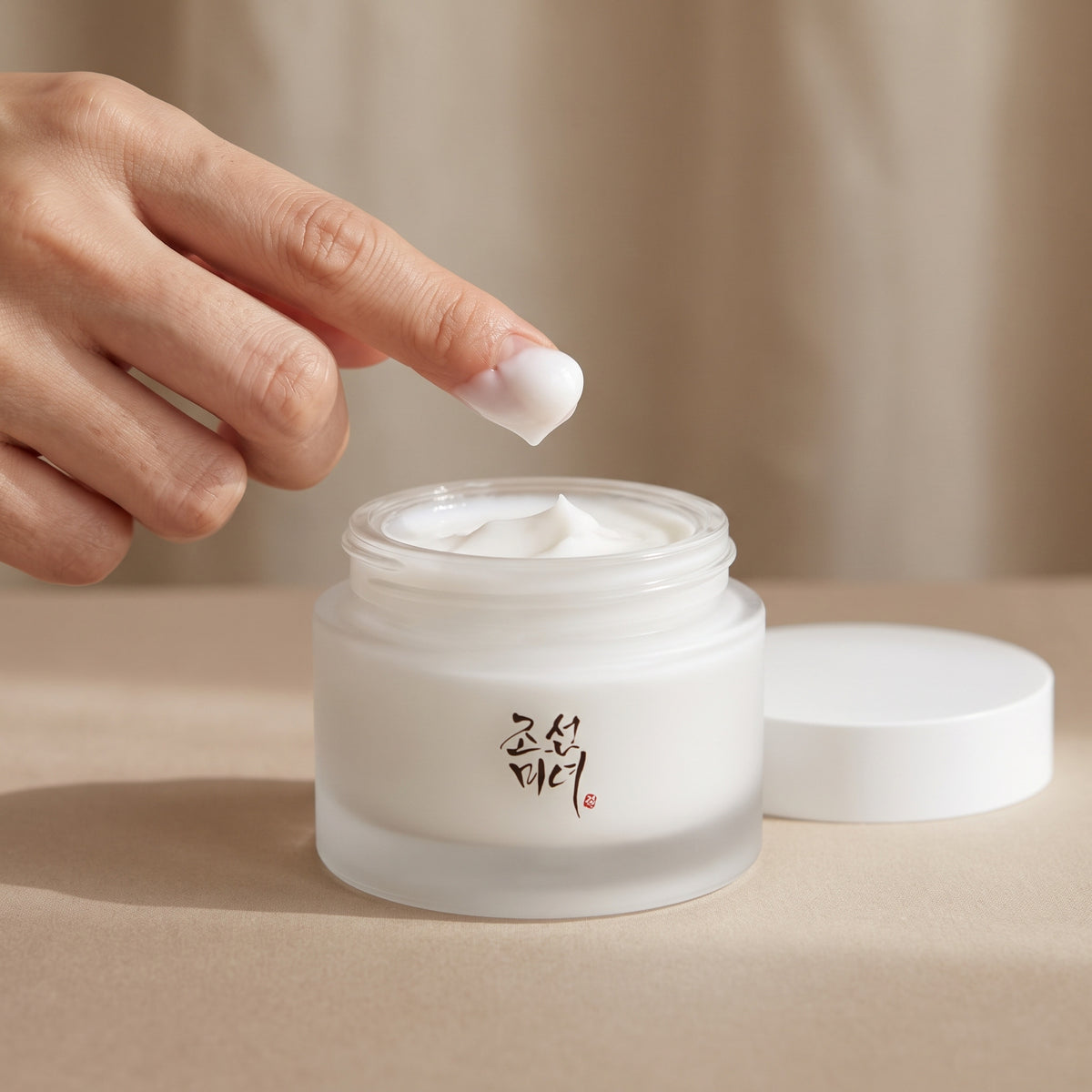 Fingertip lifting thick white BEAUTY OF JOSEON Dynasty Cream from its frosted glass jar