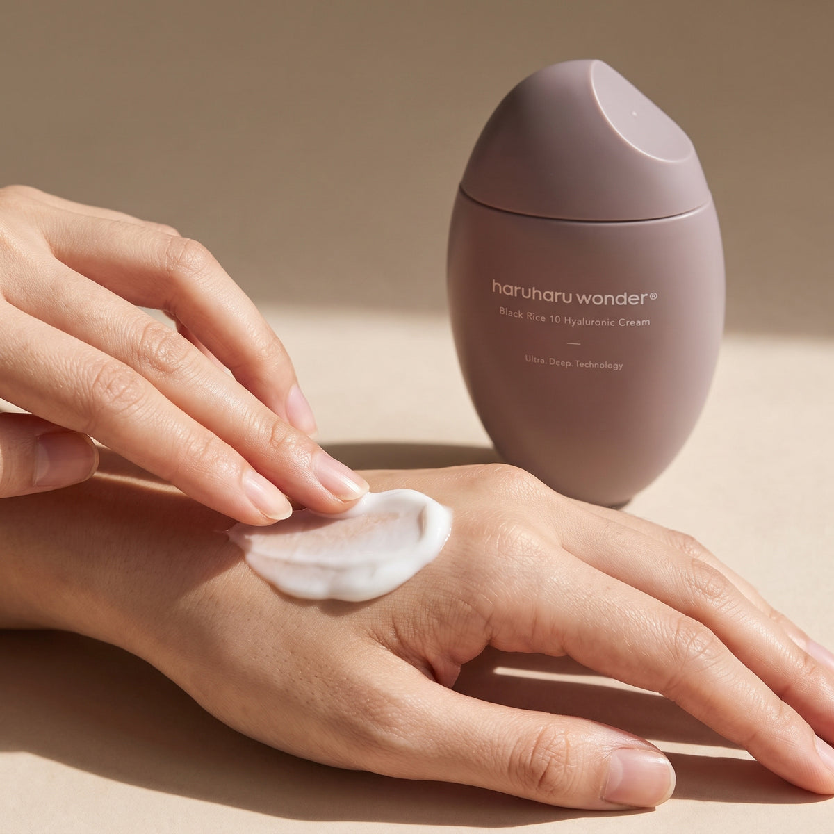 Rich white HARUHARU WONDER Black Rice 10 Hyaluronic Cream smoothed across the back of a hand beside its mauve bottle