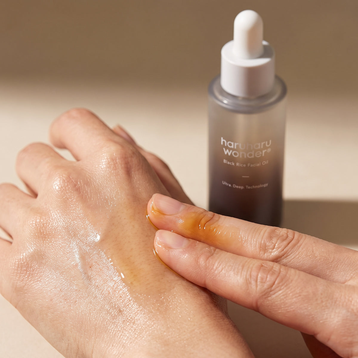 Golden HARUHARU WONDER Black Rice Facial Oil pressed into the back of a hand beside its 30ml dropper bottle