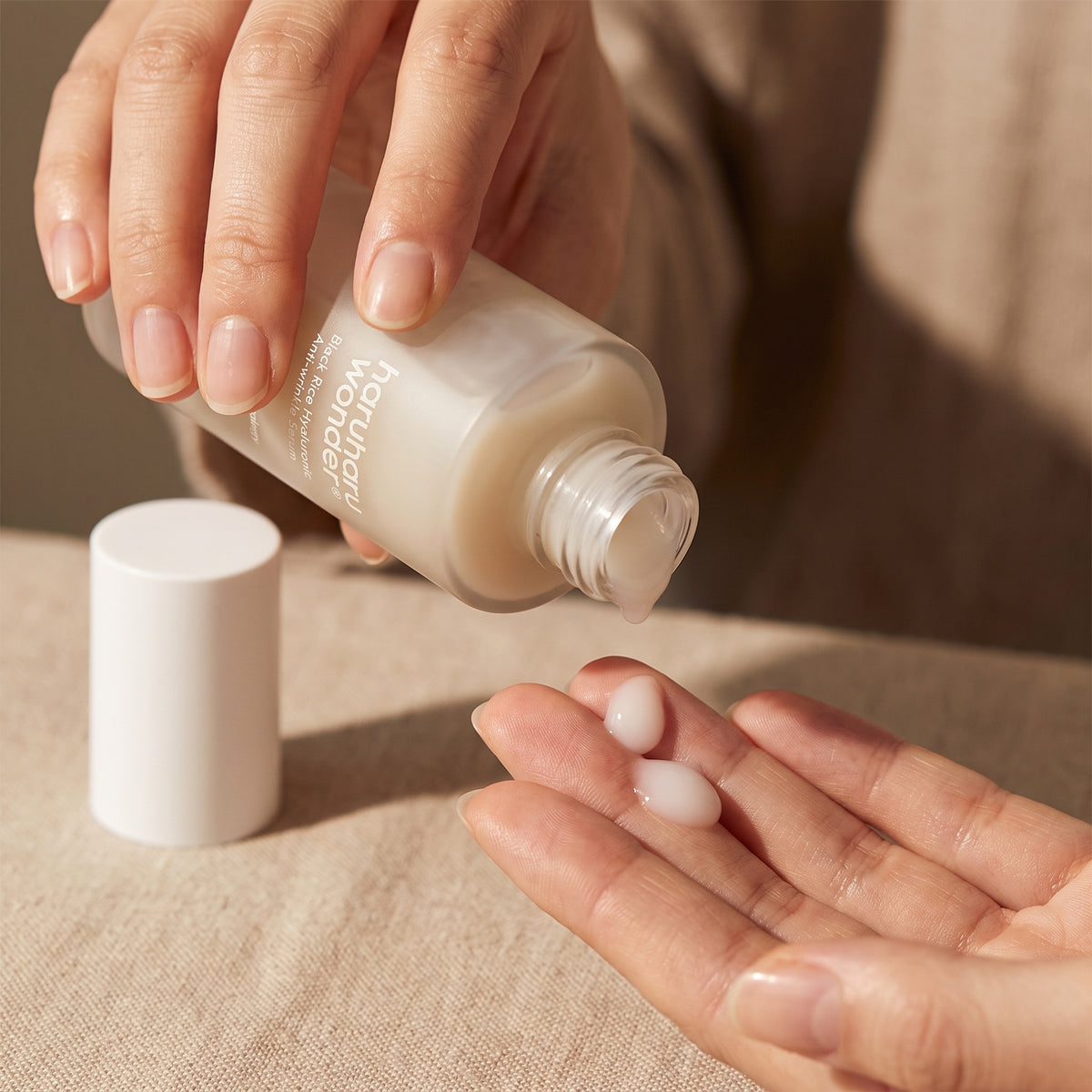 Milky HARUHARU WONDER Black Rice Hyaluronic Anti-wrinkle Serum poured from the open bottle onto fingertips